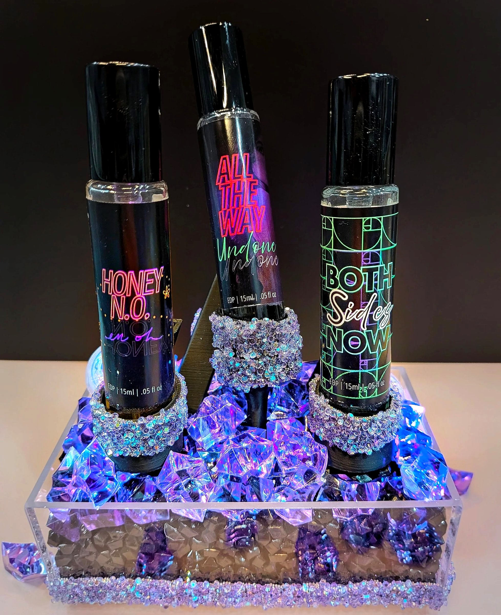 Honey N.O., All the Way Undone and Both Sides Now in 15ml bottles on a lit stand with purple crystals