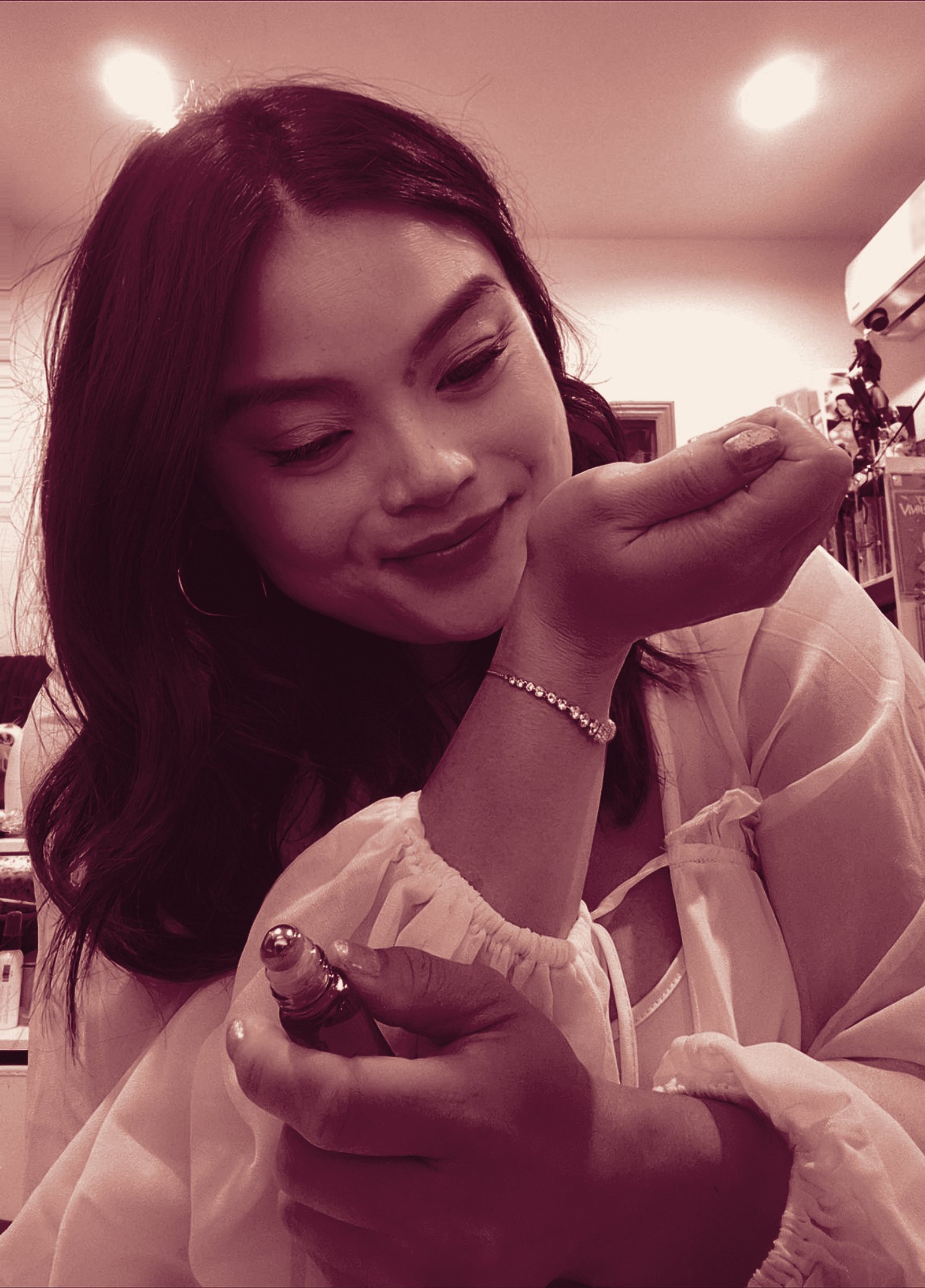 A woman smiling as she smells a perfume roller on her wrist